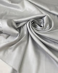Polyester satin in light gray, Glacier Gray. Very soft, light, shiny and flowy, not transparent. Ideal for dresses, skirts, blouses, and shirting. High-quality deadstock collected in Stock from a Maison de Couture in Italy.