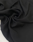Black polyester crêpe with a fluid drape and slightly textured matte surface ideal for dresses trousers and soft tailoring. High-quality deadstock collected in Stock from a Maison de Couture in Italy.