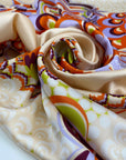 Printed polyester twill in panels. The ground is light peach and the print is in shades of bright orange, lilac, and green. Very flowy, a little shiny. High-quality deadstock collected in Stock from a Maison de Couture in Italy.