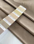 Polyester satin in gold, color reference Gravel, slightly stiff with a shiny surface and shape-holding structure. Ideal for jackets, trenches, and skirts. High-quality deadstock collected in Stock from a Maison de Couture in Italy.
