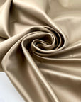 Polyester satin in gold, color reference Gravel, slightly stiff with a shiny surface and shape-holding structure. Ideal for jackets, trenches, and skirts. High-quality deadstock collected in Stock from a Maison de Couture in Italy.