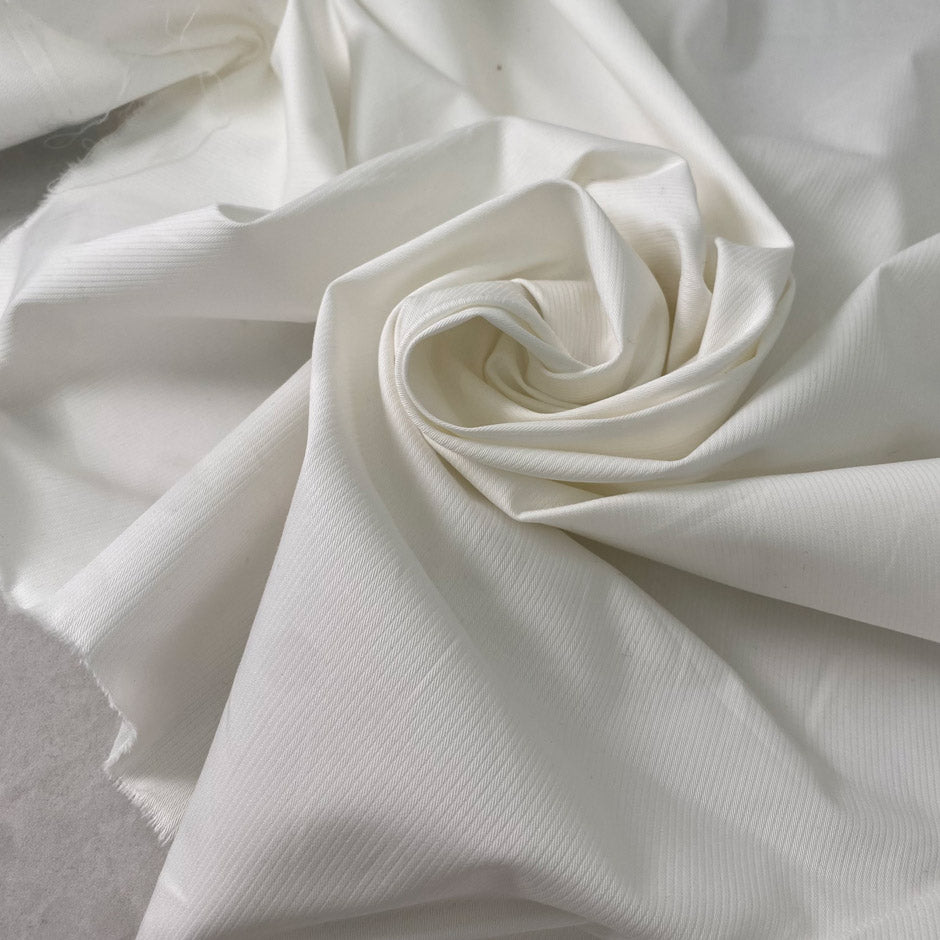 White cotton with elastane in cloudy dancer shade medium weight slightly stiff with striped texture ideal for skirts trousers and jackets. High-quality deadstock collected in Stock from a Maison de Couture in Italy.