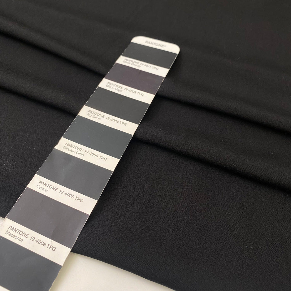 Black polyester crêpe with a fluid drape and slightly textured matte surface ideal for dresses trousers and soft tailoring. High-quality deadstock collected in Stock from a Maison de Couture in Italy.