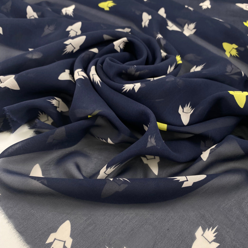 Pure silk chiffon, the ground is dark blue printed with rockets in white and bright yellow. The fabric is very soft and transparent. High-quality deadstock fabric collected in Stock from a Maison de Couture in Italy.