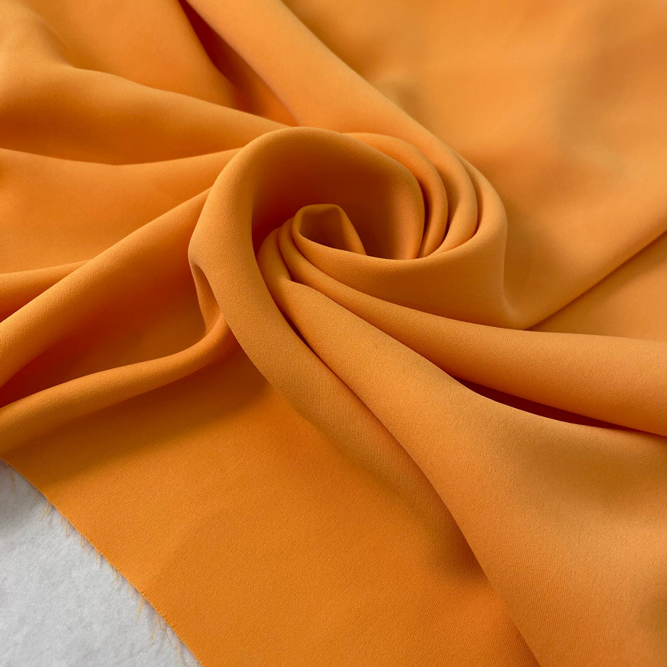 Medium-weight polyester cady in Iceland orange. Puffy, very soft and flowy, not transparent. Ideal for trousers, skirts, dresses, and heavy blouses. High-quality deadstock collected in Stock from a Maison de Couture in Italy.