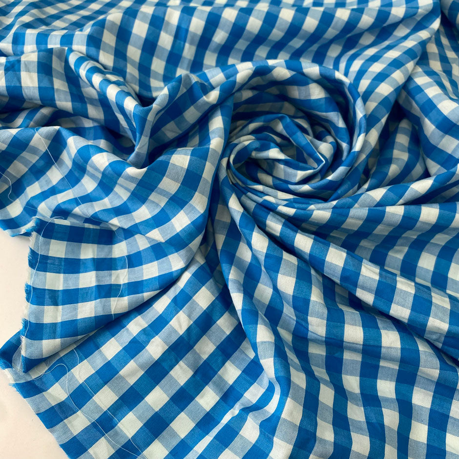 Pure cotton poplin with a small check design, approximately one centimeter squares, in light blue color reference Bu Blue. Very soft, light, flowy, and not transparent. Ideal for shirting, dresses, and skirts. High-quality deadstock collected in Stock from a Maison de Couture in Italy.