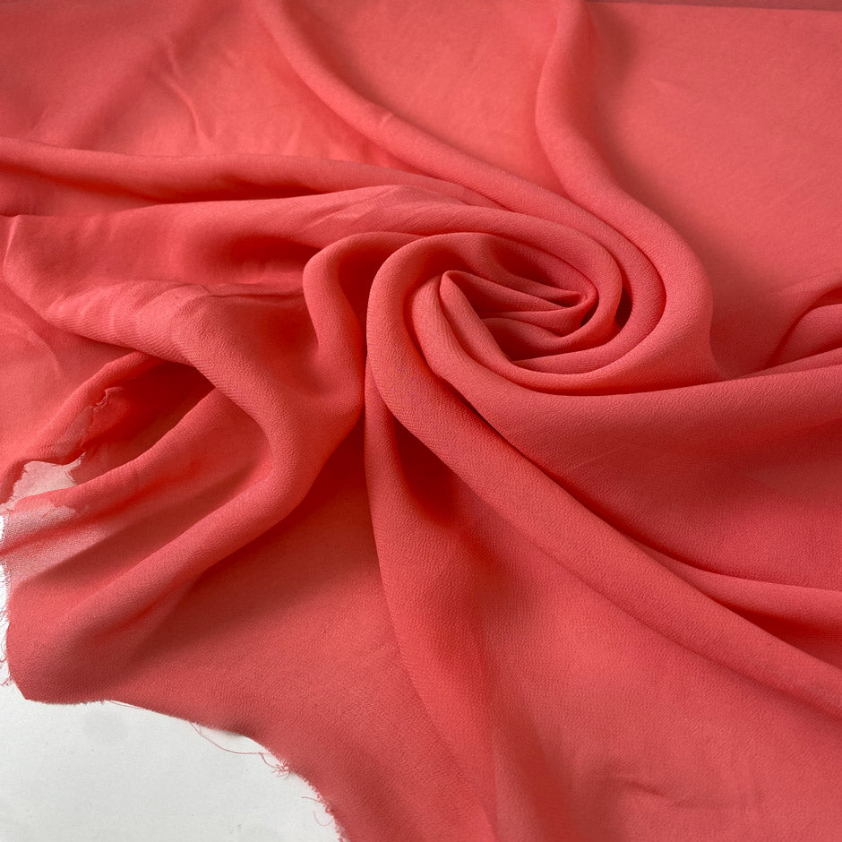 Light and soft viscose georgette in a coral shade. Slightly transparent with an elegant drape, perfect for skirts, blouses, shirting, and dresses. High-quality deadstock collected in Stock from a Maison de Couture in Italy.