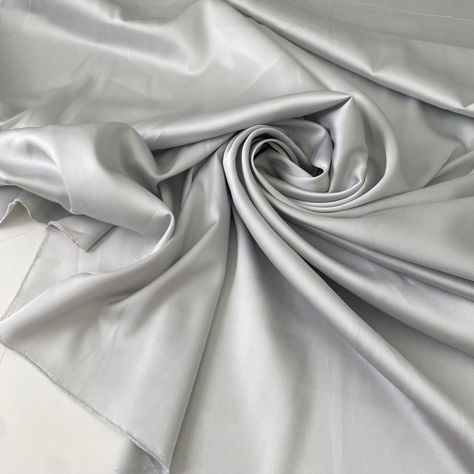 Polyester satin in light gray, Glacier Gray. Very soft, light, shiny and flowy, not transparent. Ideal for dresses, skirts, blouses, and shirting. High-quality deadstock collected in Stock from a Maison de Couture in Italy.