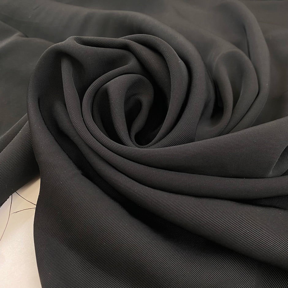 Polyester cady in black color reference Pirate Black. Very soft and flowy, not transparent, ideal for trousers, skirts, and dresses. High-quality deadstock collected in Stock from a Maison de Couture in Italy.