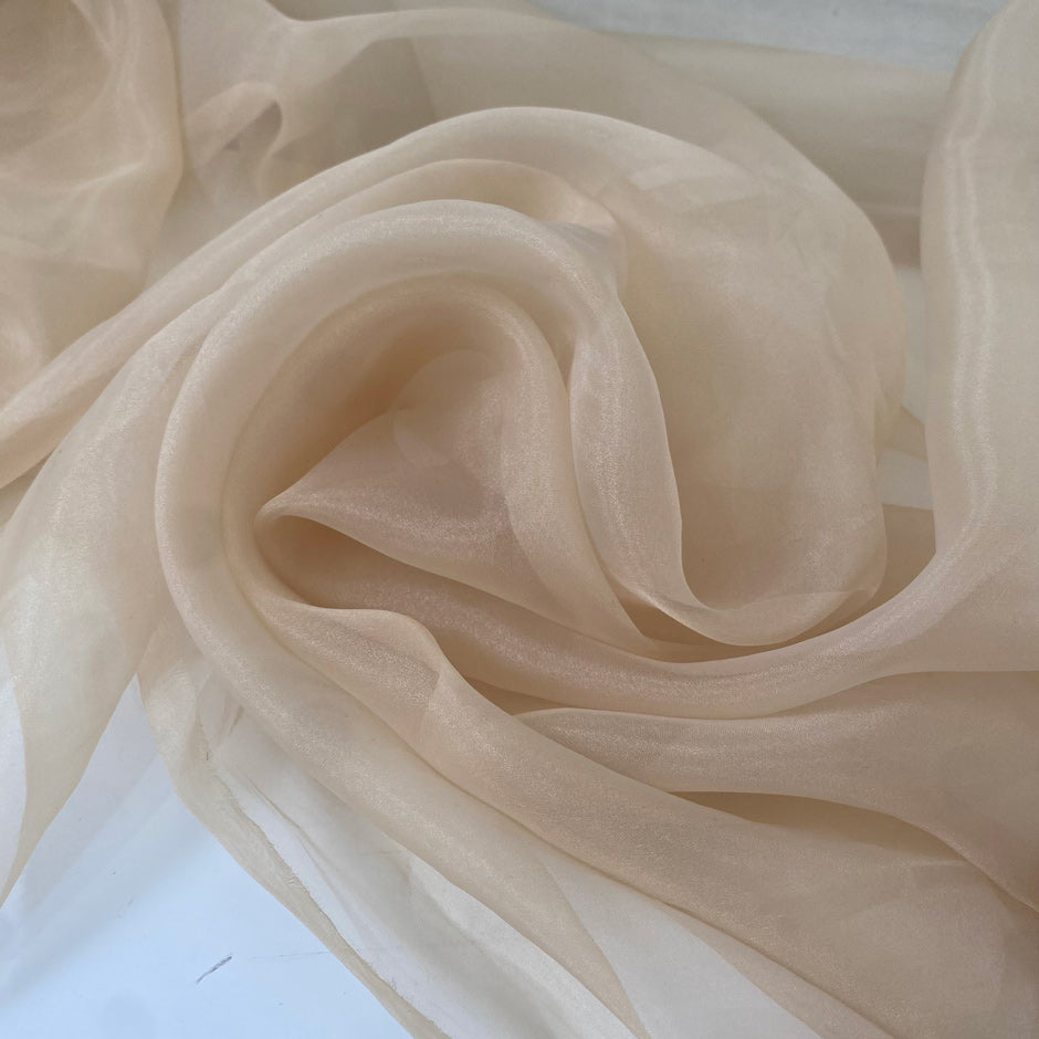 Light and transparent polyester organza in a shiny beige tone. Ideal for dresses, skirts, blouses, and shirting. High-quality deadstock collected in Stock from a Maison de Couture in Italy.