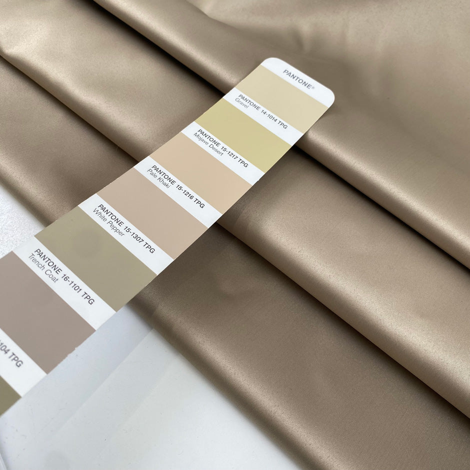 Polyester satin in gold, color reference Gravel, slightly stiff with a shiny surface and shape-holding structure. Ideal for jackets, trenches, and skirts. High-quality deadstock collected in Stock from a Maison de Couture in Italy.