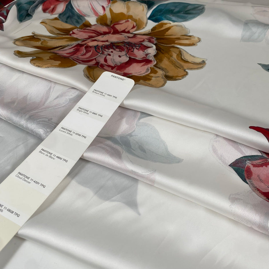 Polyester satin with a white base and large floral print in red, green, gray, pink, and beige. Light, flowy, slightly shiny, not transparent. High-quality deadstock collected in Stock from a Maison de Couture in Italy.