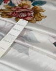 Polyester satin with a white base and large floral print in red, green, gray, pink, and beige. Light, flowy, slightly shiny, not transparent. High-quality deadstock collected in Stock from a Maison de Couture in Italy.