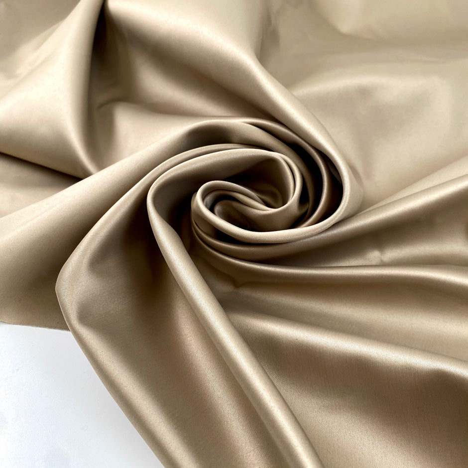 Polyester satin in gold, color reference Gravel, slightly stiff with a shiny surface and shape-holding structure. Ideal for jackets, trenches, and skirts. High-quality deadstock collected in Stock from a Maison de Couture in Italy.