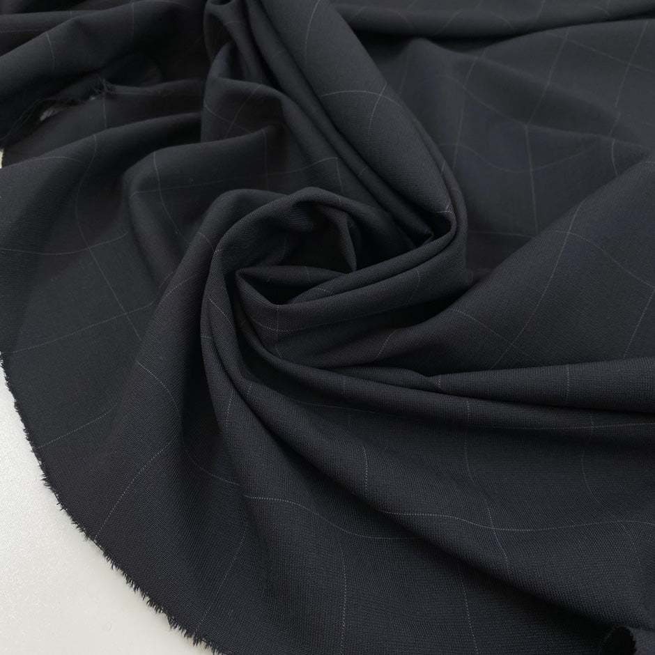 Wool mixed with polyester and elastane featuring a check design in dark blue. Very soft, light, flowy, and not transparent. Ideal for trousers, skirts, and jackets. High-quality deadstock collected in Stock from a Maison de Couture in Italy.